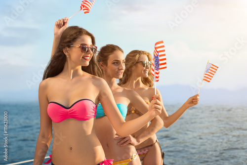 Smiling girls hold american flags. Attractive women on sea background. Greetings from USA. Happiness and freedom.