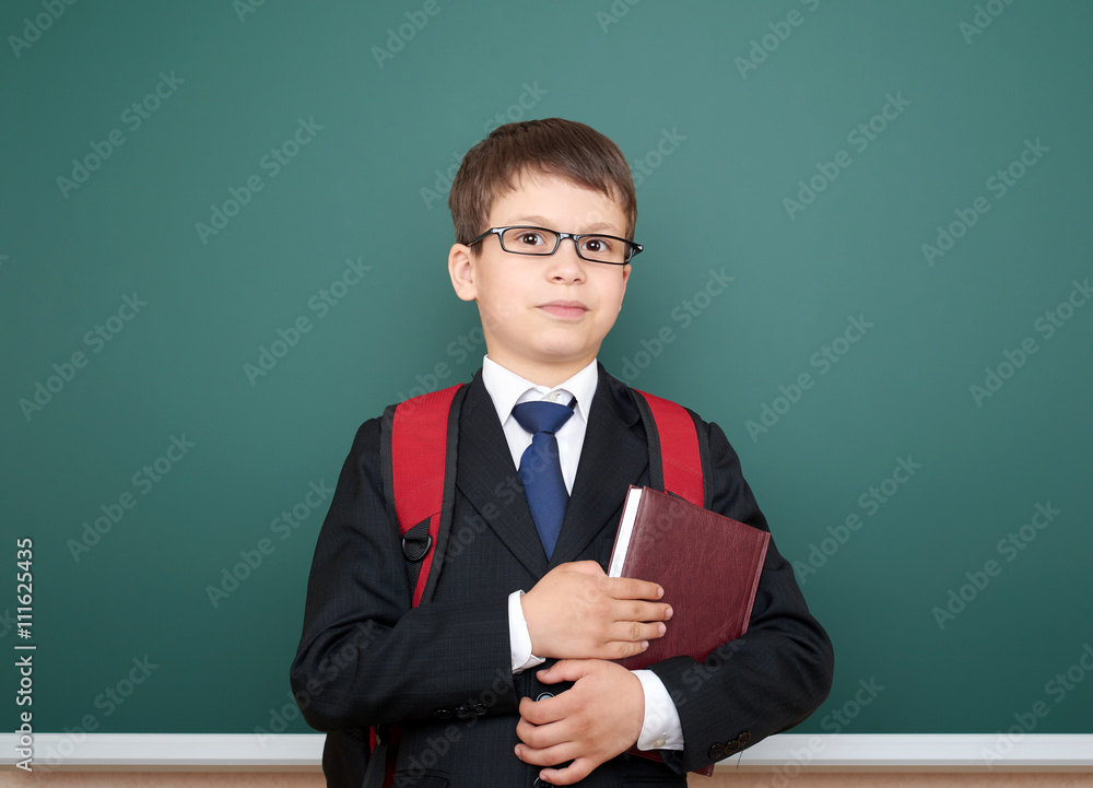 school boy portrait in black suit on green chalkboard background with red backpack and book, education concept school boy portrait in black suit on green chalkboard background with red backpack and book, education concept