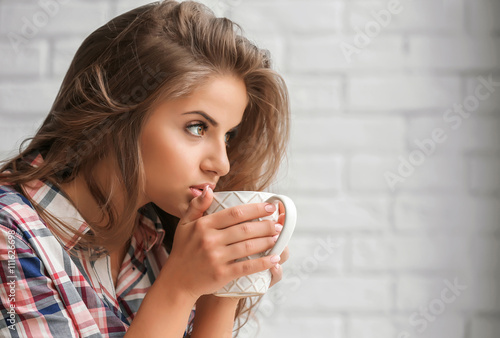 Fototapeta Naklejka Na Ścianę i Meble -  Beautiful young woman holding cup on brick wall background