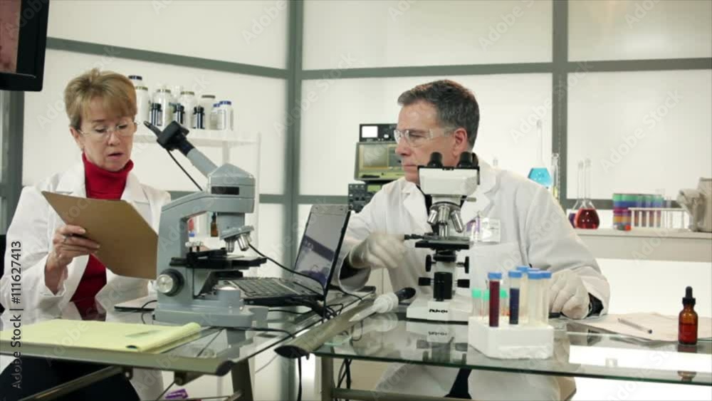 A male and a female researcher or scientist sitting in a laboratory discussing reports or findings. A male and a female researcher or scientist sitting in a laboratory discussing reports or findings.