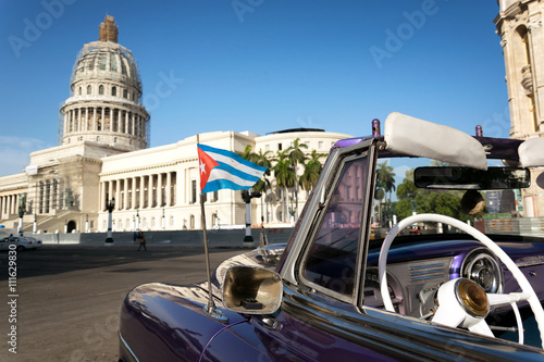 Cuban flag on a classic car with the Capitolio on the background in Havana, Cuba
