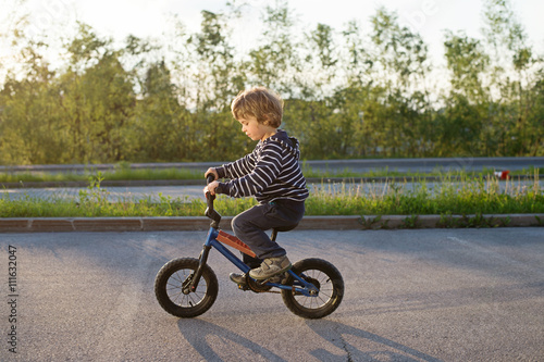 Little boy in striped sweater without protection helmet riding small bike. Children outdoors activities, recreation.