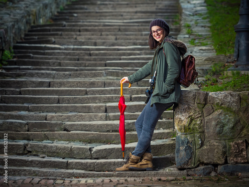 Young hipster woman is standing on the stairs of the fortress in an old town. She is ready for sightseeing even if it is going to rain.