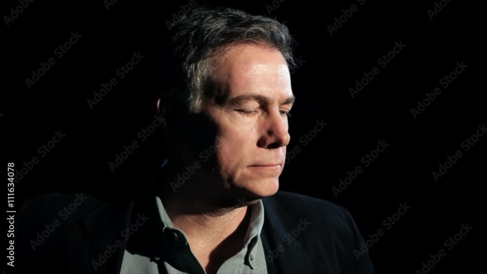 A dark backdrop and harsh lighting frames a mature man who appears rather melancholy. A dark backdrop and harsh lighting frames a mature man who appears rather melancholy.