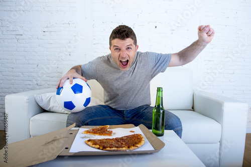 young man holding ball watching football game on tv at home couch with pizza and beer celebrating crazy goal or victory © Wordley Calvo Stock