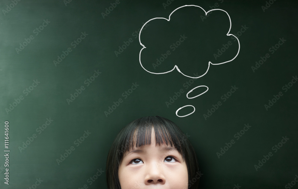 Cute thinking kid girl  with empty bubble looking on the blackboard background.