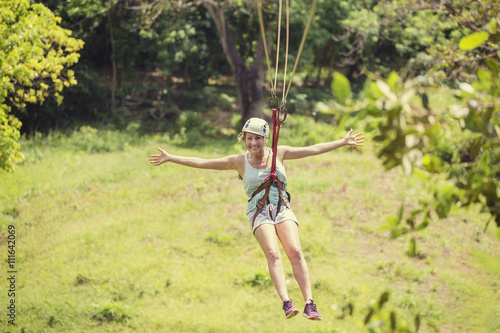 Happy woman riding a zip line in a lush tropical forest. Having fun with arms outstretched