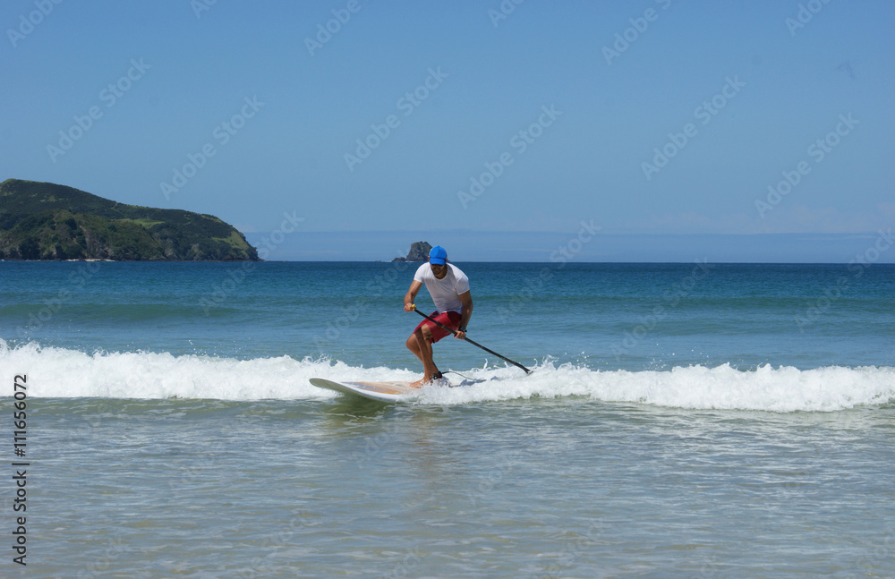 Paddleboarder on a SUP surfing a wave. Paddle boarder photographed in Northland, New Zealand. Paddleboarder on a SUP surfing a wave. Paddle boarder photographed in Northland, New Zealand.