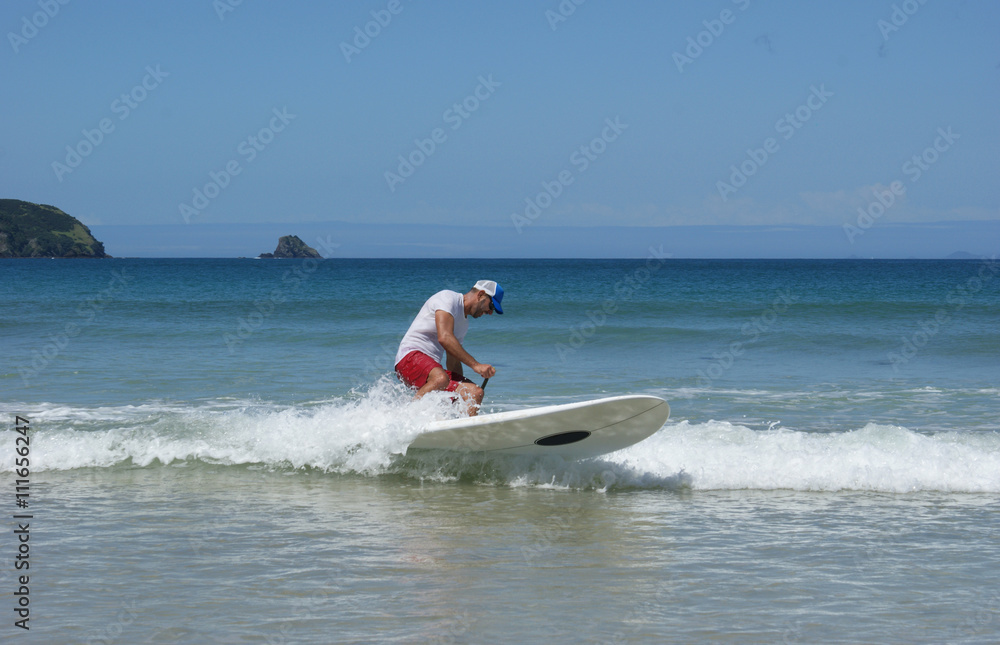 Paddleboarder on a SUP surfing a wave. Paddle boarder photographed in Northland, New Zealand. Paddleboarder on a SUP surfing a wave. Paddle boarder photographed in Northland, New Zealand.