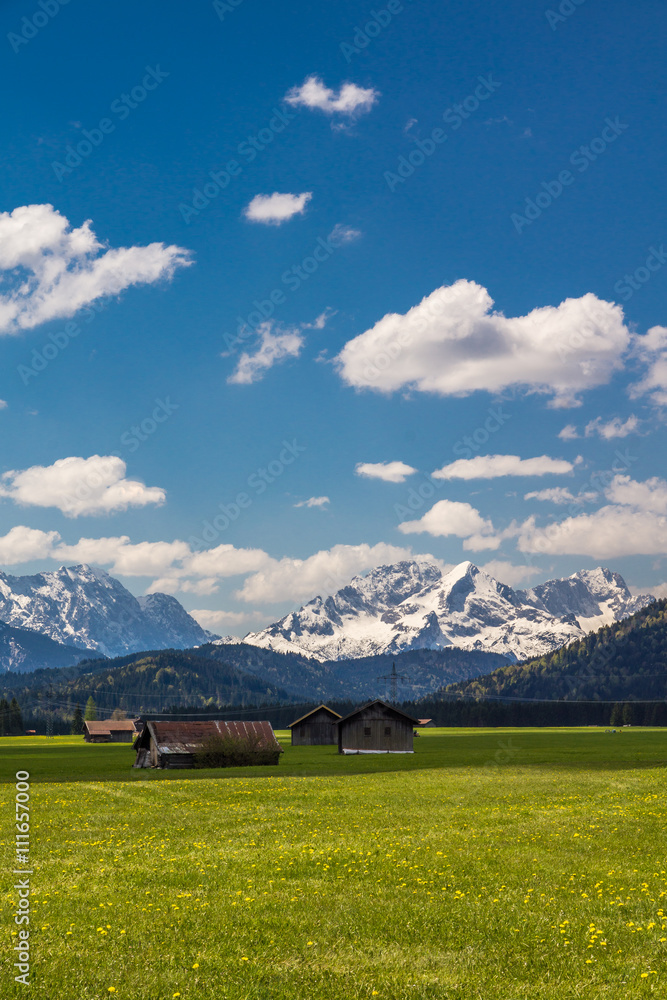 Holzhütten auf einer Almwiese vor dem Bergmassiv des Wettersteingebirges