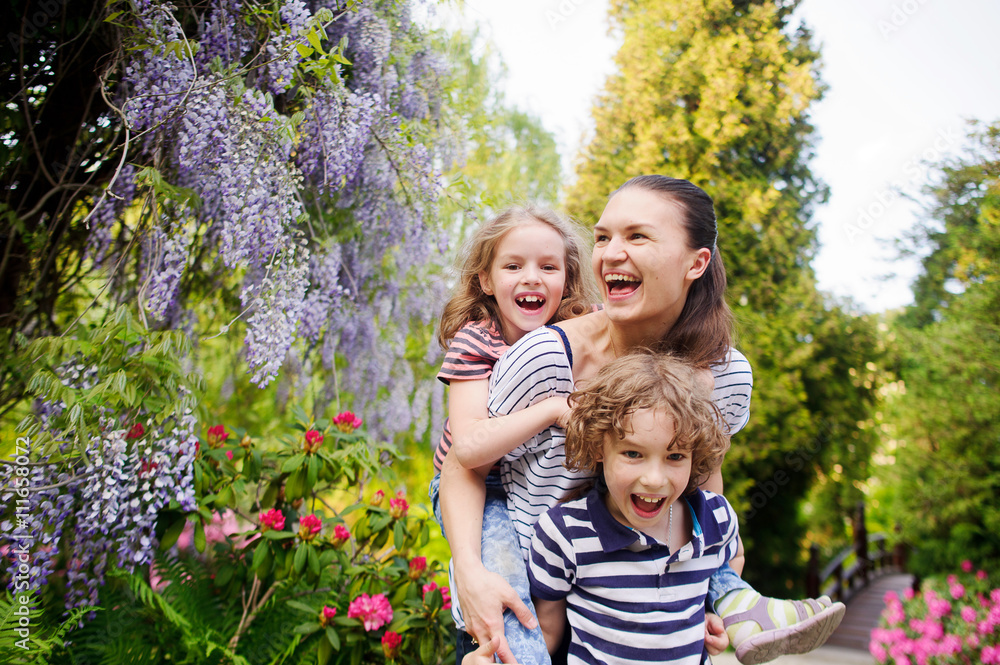 Fototapeta premium Young woman with her daughter and son on a background of blossoming garden
