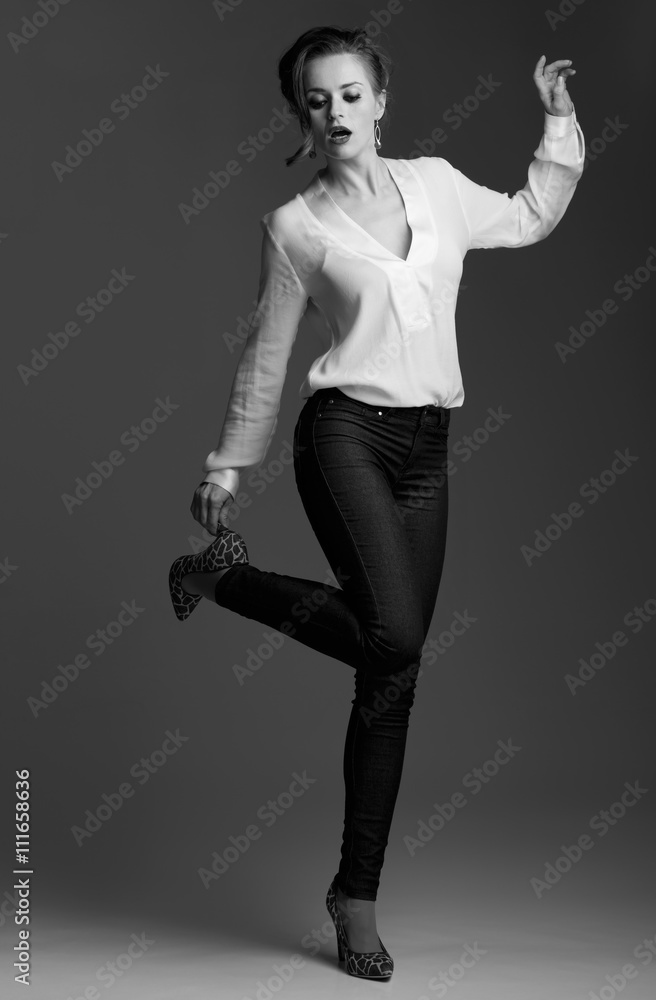 Modern elegant woman adjusting shoe against grey background