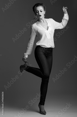 Modern elegant woman adjusting shoe against grey background
