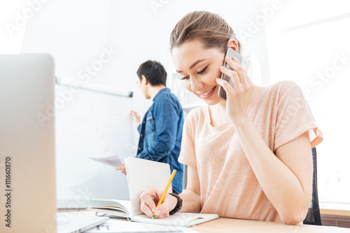 Cheerful woman talking on cell phone in office