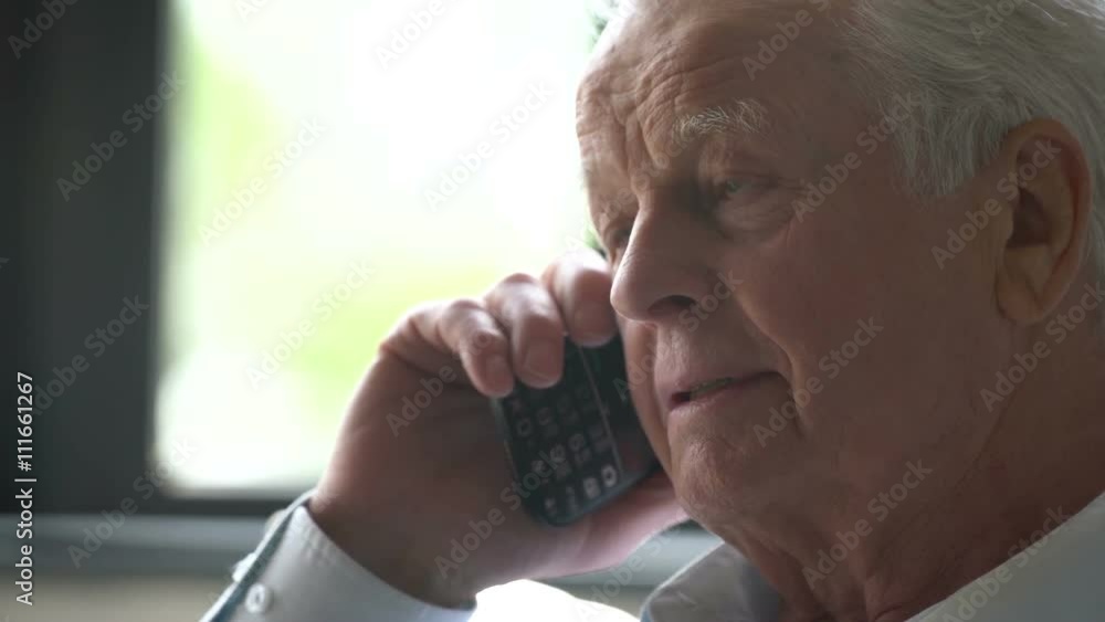 elderly man sits in a chair and speak at phone in a modern apartment elderly man sits in a chair and speak at phone in a modern apartment