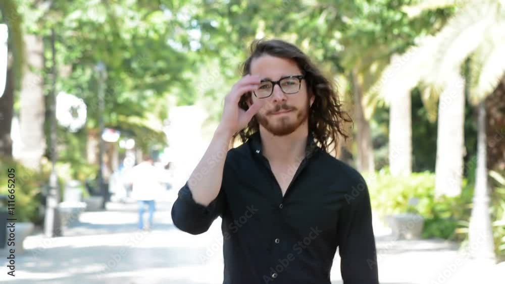 Young man walks toward the camera. Portrait in a park. Middle twenties. Long hair, blue eyes and glasses. Young man walks toward the camera. Portrait in a park. Middle twenties. Long hair, blue eyes and glasses.