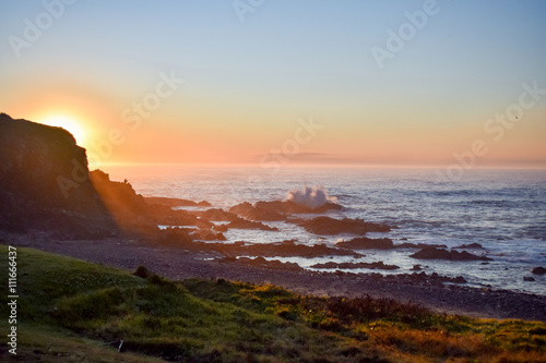 Silhouette of man fishing whilst sitting on coastal rocks in the early hours of morning