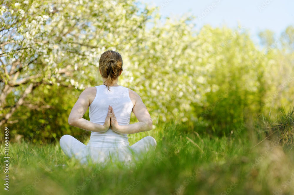 Young woman in a lotus position in a flourishing park.
