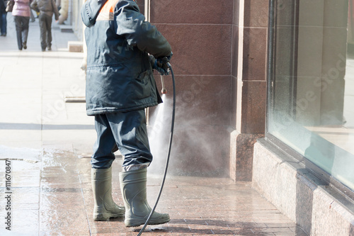 the person washes the sidewalk from a hose before show-window of shop