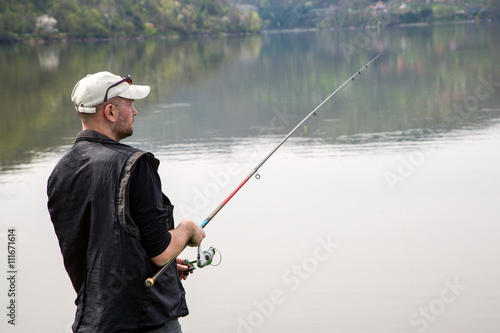 Side View Of Fisherman Reeling String And Throwing Rod In The Calm Lake, Half-Length Shot