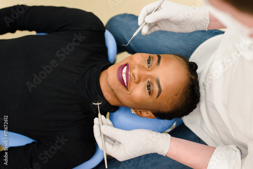 Young African-American ethnic black female smiling while dentist in white latex gloves check condition of her teeth