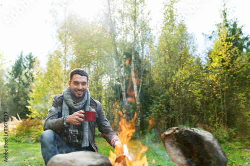 happy man drinking hot tea near camp fire