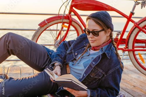 young woman with vintage bicycle resting and reading a book on seaside © kurapatka