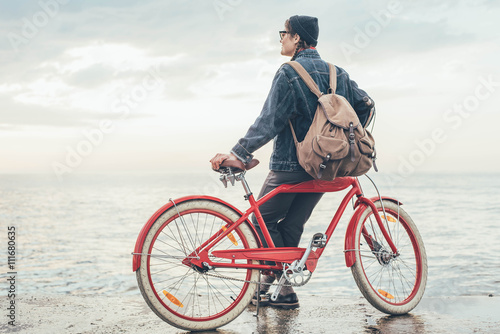 Fototapeta Naklejka Na Ścianę i Meble -  woman with vintage bicycle looking at view on seaside during sunset or sunrise