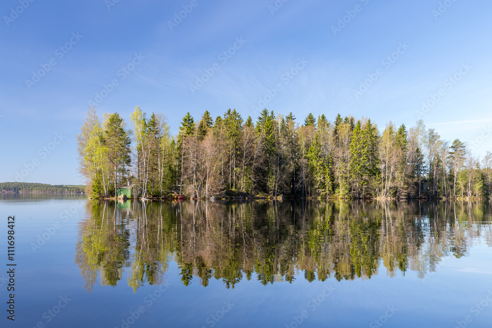 Island in calm lake on sunny day Island in calm lake on sunny day
