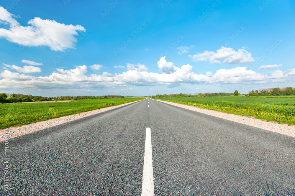 Asphalt road in green fields on blue cloudy sky background