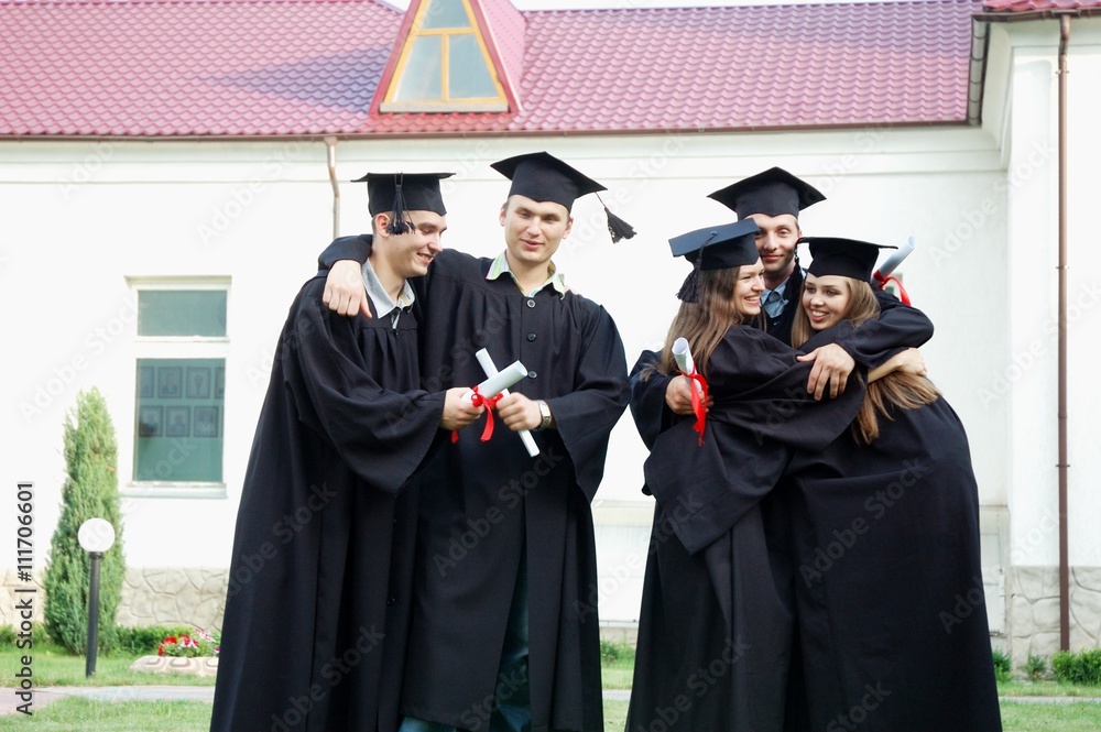 Graduates with diplomas in their hands happily embrace each other