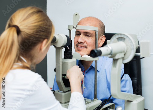 Fototapeta Naklejka Na Ścianę i Meble -  Friendly female optician doing eye examination with lamp