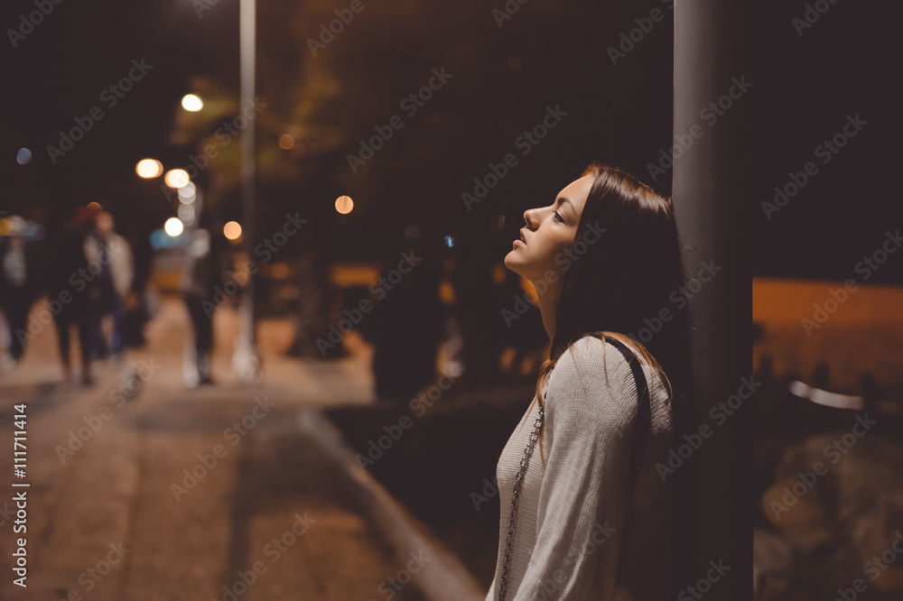 Portrait of beautiful young lady looking up, city street in the night, evening lights bokeh background outdoors Portrait of beautiful young lady looking up, city street in the night, evening lights bokeh background outdoors