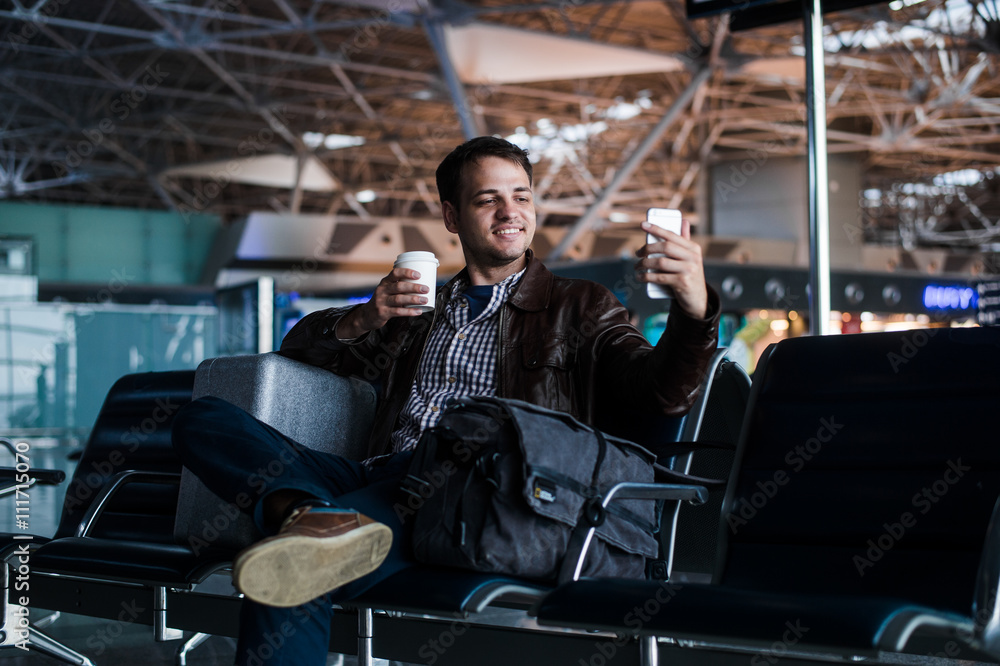 Portrait of a young man laughing and taking selfie with coffee at the airport waiting his flight Portrait of a young man laughing and taking selfie with coffee at the airport waiting his flight