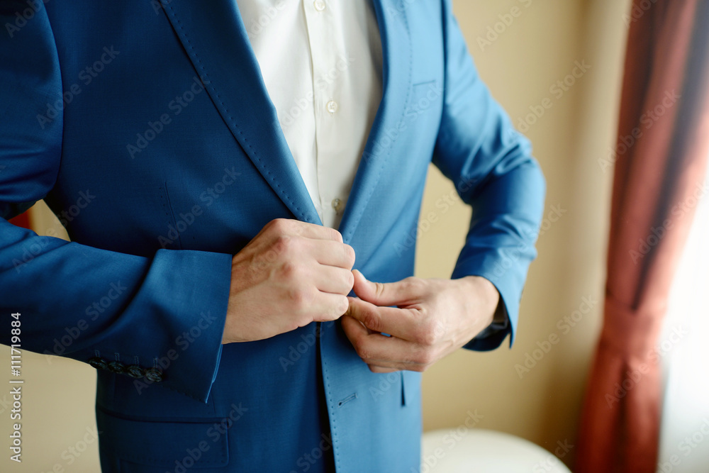 Groom is wearing a suit indoors. Male portrait of handsome guy. Beautiful model boy in colorful wedding clothes. Man is posing