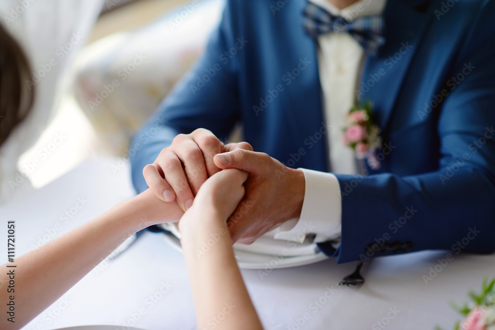 Wedding couple is holding hands. Beauty bride with groom. Beautiful model girl in white dress. Man in suit. Female and male portrait. Close-up woman's arms. Cute lady and guy indoors