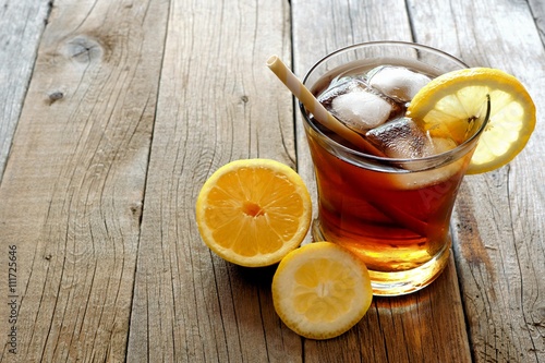 Glass of homemade lemon iced tea with straw on a rustic wooden background