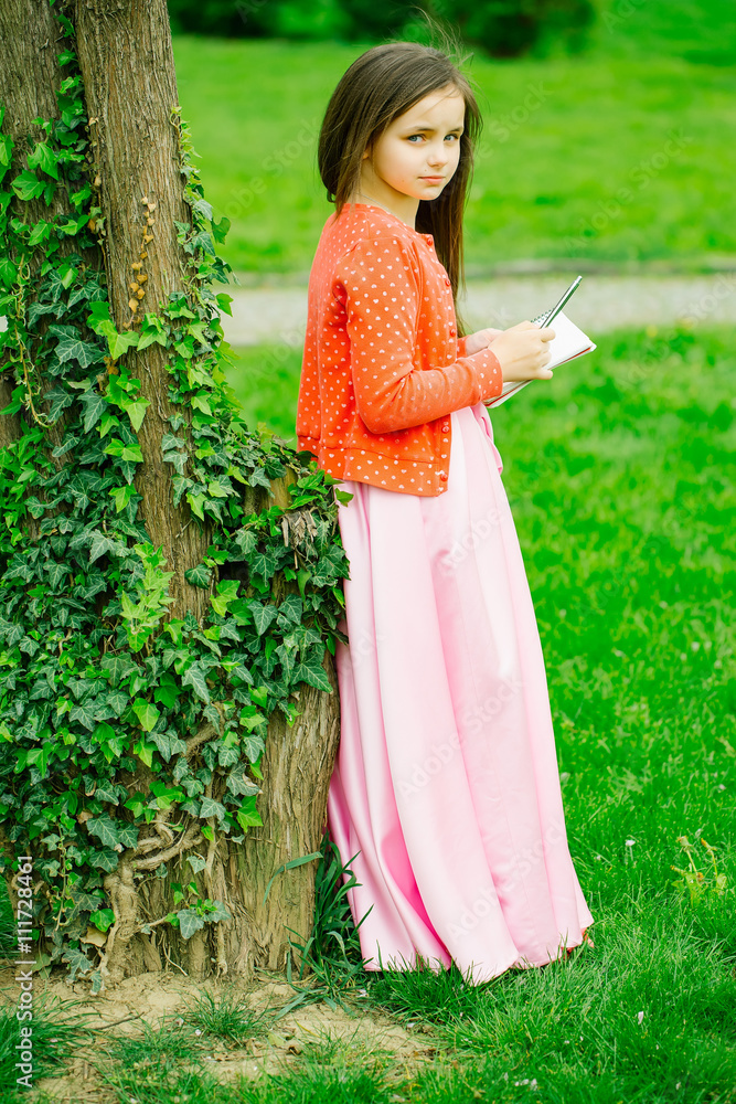 Naklejka premium Girl in dress with notebook and pen near tree