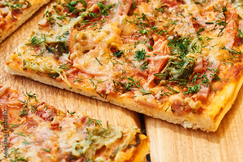 Slices of a traditional pizza with ham, cheese and tomatoes sprinkled with greens closeup