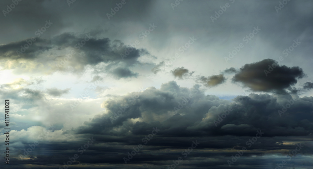 Fototapeta premium Dark clouds in the sky reaching toward the horizon before the rain illuminated by the setting sun.