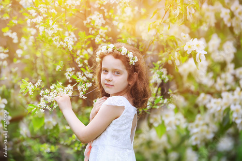 Little girl in white dress near blooming cherry trees.