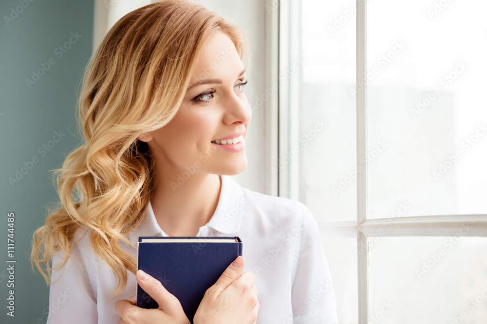 Fototapeta premium Pretty young reader holding book and looking in window