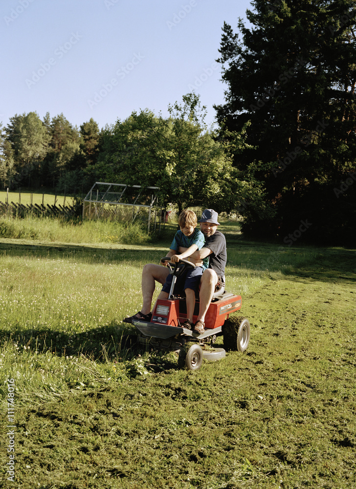 A father and son on a lawnmower. A father and son on a lawnmower.