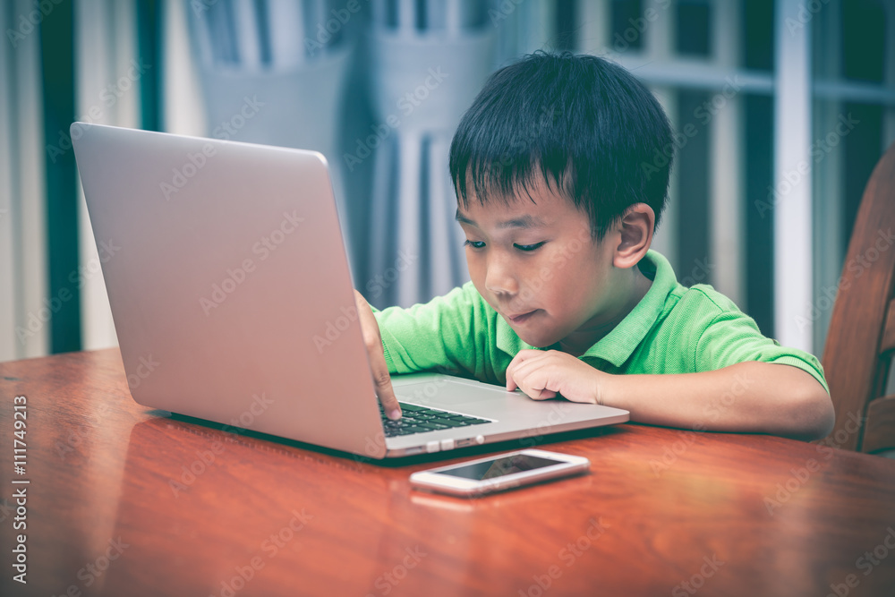 Asian boy enjoying modern generation technologies playing indoor using laptop and mobile phone. Asian boy enjoying modern generation technologies playing indoor using laptop and mobile phone.