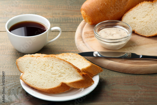 cut the baguette with a knife on wooden cutting Board on wooden background with sauce and a Cup of strong coffee