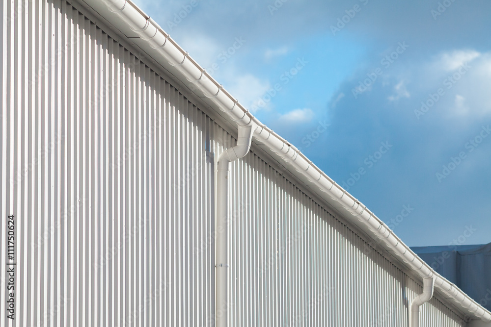 New white rain gutter on a building with white metal sheet against blue sky New white rain gutter on a building with white metal sheet against blue sky