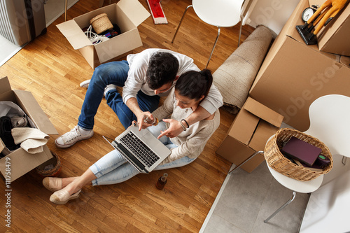 Young couple Moving in new home.Sitting on floor and relaxing after cleaning and unpacking.Looking something on laptop.