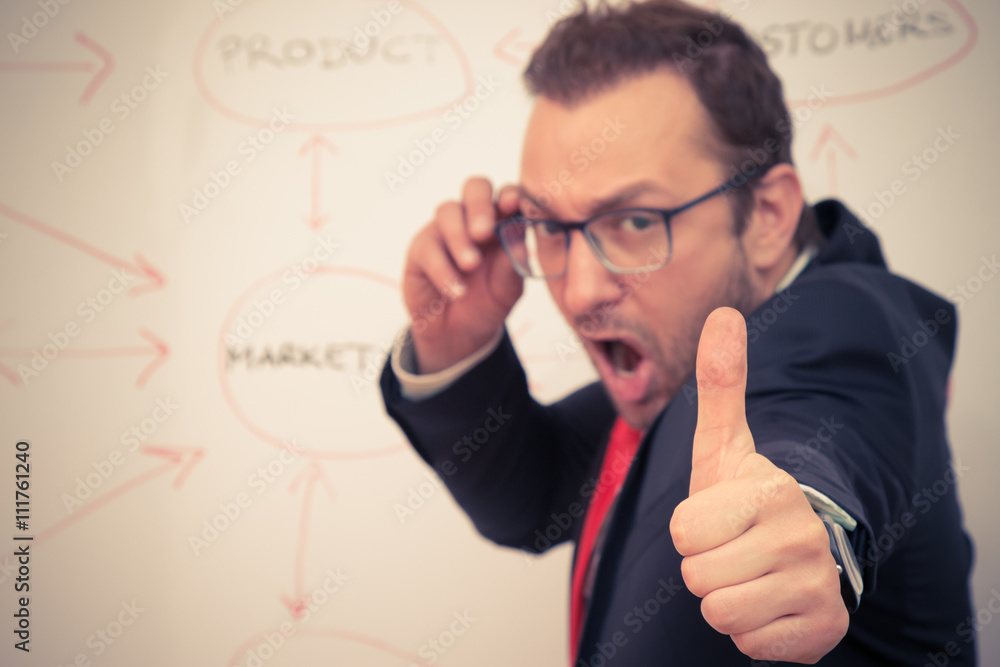 Cheerful businessman with thumbs up gesture in front of the white board with flowchart. Selective focus. Business success concept. Cheerful businessman with thumbs up gesture in front of the white board with flowchart. Selective focus. Business success concept.