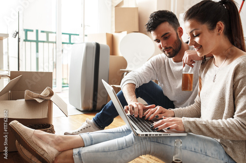 Young couple Moving in new home.Sitting on floor and relaxing after cleaning and unpacking.Looking something on laptop.