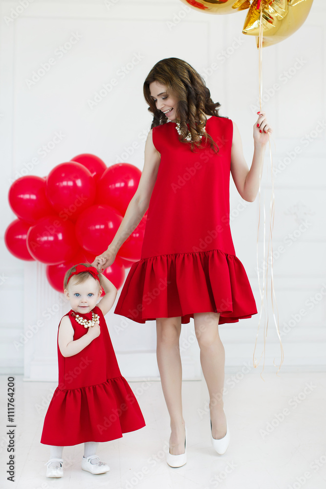 Portrait of a mother with a young daughter and balloons,mom-brunette with long curly hair and a little girl with short hair with a red bow on her head,dressed in a red dress and pearl necklace Portrait of a mother with a young daughter and balloons,mom-brunette with long curly hair and a little girl with short hair with a red bow on her head,dressed in a red dress and pearl necklace